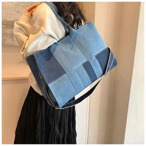 Detail of a large denim tote bag featuring patchwork fabric and reinforced shoulder straps