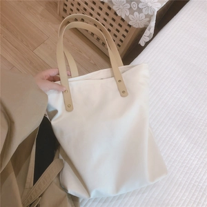 Detail of white canvas tote bag featuring beige leather handles and gold metal rivets