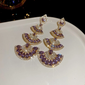 Close-up of fan-shaped purple crystal pendant earrings with gold tassels on white ceramic