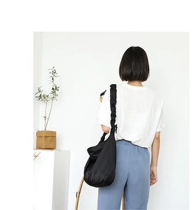 Detail of black crossbody bag featuring pleated shoulder strap on model's back