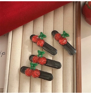 Detailed view of four cherry hair clips with red sequins on a beige jewelry tray