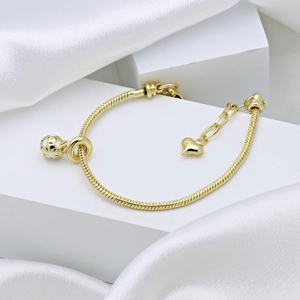 Elegant gold snake chain bracelet with white polka dot charm and heart pendant detail