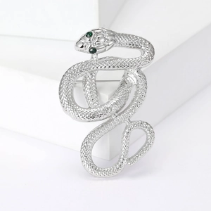 Detail of silver snake brooch featuring scale texture and green gemstone eyes on white stand
