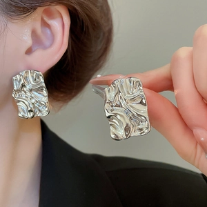 Close-up of silver square stud earrings featuring irregular pleated liquid metal texture