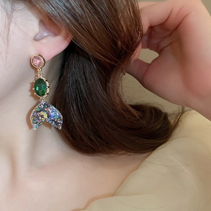 Close-up of mermaid tail drop earring with pink and green gems on model's ear