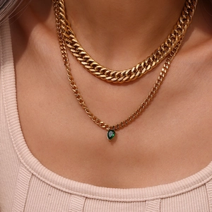 Detail of layered gold Cuban chain necklace with green waterdrop zircon pendant on model