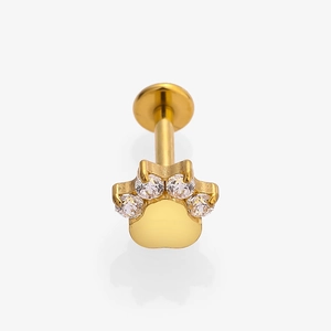Close-up of golden titanium labret stud with crystal paw print design on white background