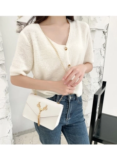 White envelope crossbody bag with gold deer tassel detail shown on a model