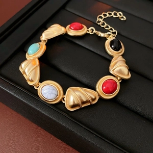 Macro shot of vintage gold bracelet with colorful oval gemstones on a black leather pad