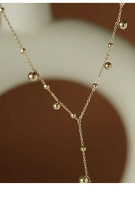 Macro detail of 18k gold plated Y-shaped necklace with polished beads on a thin chain