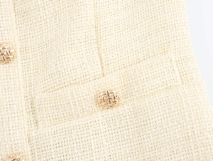 Detailaufnahme von beigem Tweed-Stoff mit goldenen geflochtenen Knöpfen und Taschen