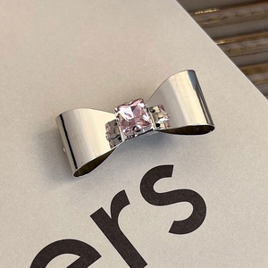 Macro view of silver bow hair clip with pink princess-cut gemstone and clear crystals