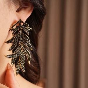 Detailed view of vintage gold leaf earrings with black rhinestones on a female model