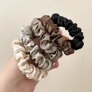 Close-up of four satin scrunchies in gold, grey, brown and black with silk texture