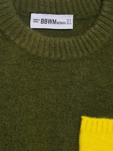 Détail d'un pull en maille vert foncé avec étiquette blanche et empiècement jaune vif