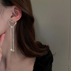 Détail de boucles d'oreilles pendantes à cœur et strass portées par un mannequin