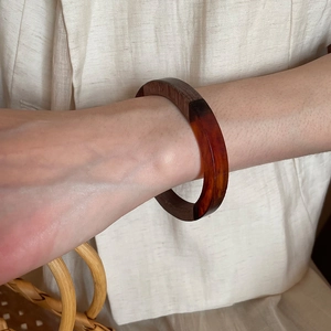 Detail of wood and resin bangle showing natural texture on beige fabric background