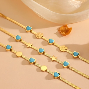 Détail de bracelets serpent dorés avec pendentifs cœur bleu et breloques trèfle à quatre