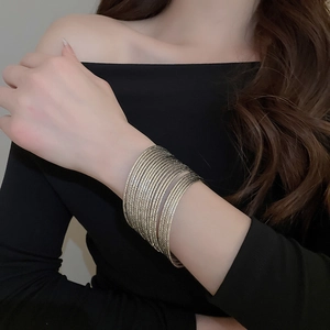 Detailed view of twenty-piece gold textured stacking bracelets on a female model wrist