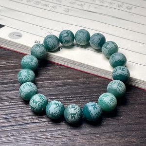 Close-up of green agate beads with carved Buddhist mantras on a wooden table
