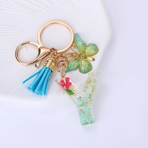 Macro detail of resin letter Y keychain with pink dried flowers, tassel and butterfly charm