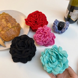 Detailed view of large fabric flower hair claws in five colors on a rustic tabletop