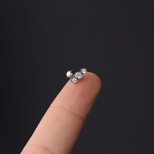 Macro shot of 16G stainless steel cartilage stud featuring three clear zircons on a fingertip