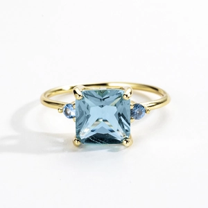 Macro shot of gold ring featuring square sky blue gem and dark blue side stones