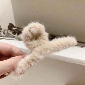 Gros plan d'une pince à cheveux en fausse fourrure beige tenue à la main pour la texture