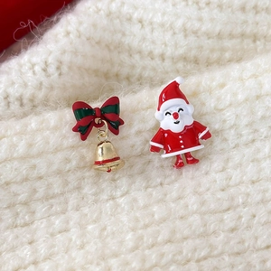Detail of Christmas stud earrings with red bow gold bell and Santa Claus on knit background