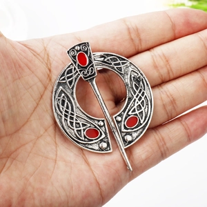 Macro view of vintage silver Viking brooch with Celtic knots and red enamel on palm