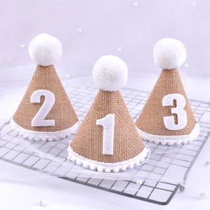 Detailed view of linen party hats with white pom poms and numbers for kids birthdays