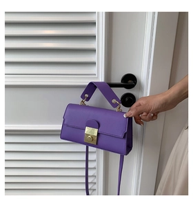 Detail view of purple leather crossbody bag with metal buckle hanging on a white door