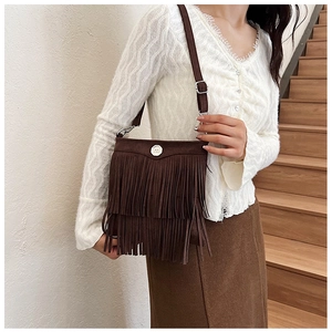 Detail of brown tassel crossbody bag with suede texture and circular decorative buckle