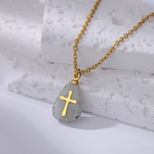 Macro view of gold cross pendant on grey teardrop natural stone with fine gold chain