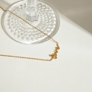 Detail of 18K gold stainless steel necklace with cursive love pendant on glass