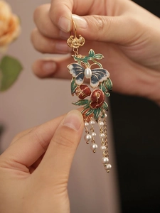 Détail de boucles d'oreilles papillon vintage avec fleurs émaillées et glands en perle