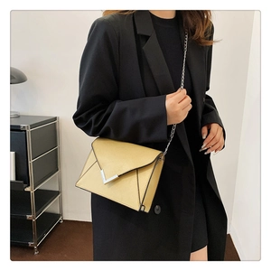 Close-up of a yellow envelope crossbody bag with silver chain strap and V-shaped buckle