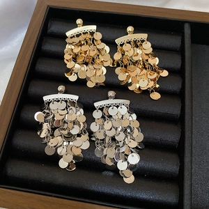Detail of layered gold and silver sequin tassel earrings on a jewelry display tray