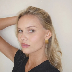 Close-up of golden rectangular earrings with a pleated texture worn by a female model
