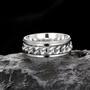 Macro detail of silver Cuban link spinner ring with industrial textured edges on black rock