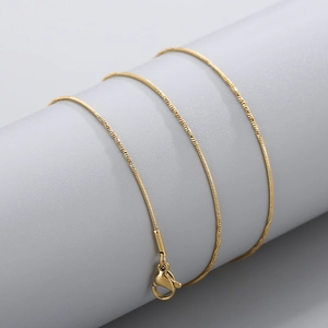 Detail of a polished gold snake bone chain with a secure lobster clasp on grey stand