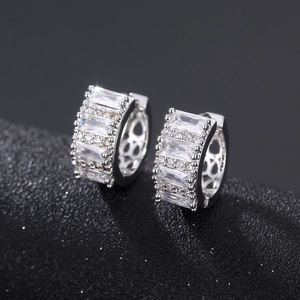 Silver baguette-cut zircon huggie earrings with pavé stones on black leather background