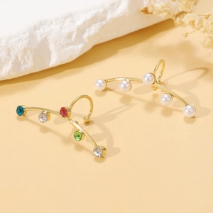 Detail of gold-plated ear cuffs with colorful rhinestones and white pearls on a stone