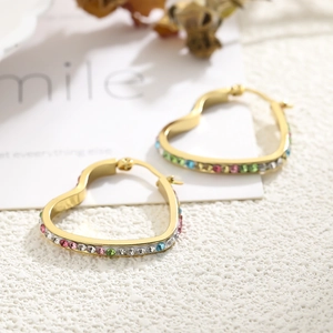 Detail view of gold hoop earrings with multi-colored crystals on a textured white background