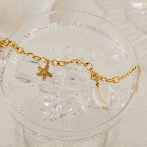 Detailed view of a gold starfish and shell bracelet draped over ice in a glass