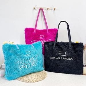 Close-up of three plush tote bags with embroidery in rose red, teal, and black