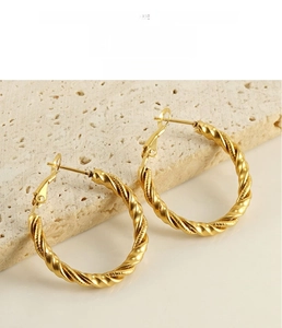 Detail of twisted rope gold hoop earrings resting on a textured minimalist stone