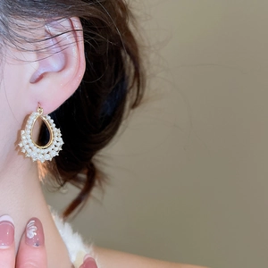 Macro view of teardrop pearl earrings with gold base and white crystal inlay on model
