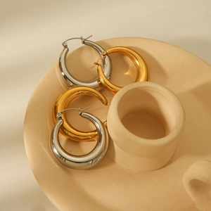 Golden and silver hollow hoop earrings with mirror finish on a ceramic display